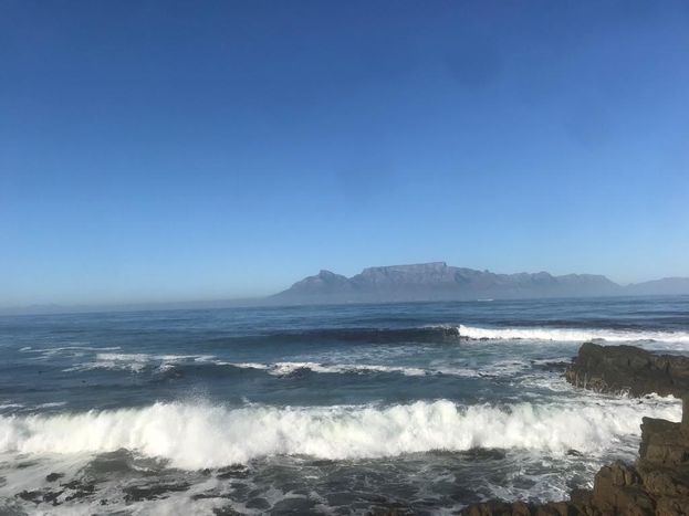 Dev dalgalar ve köpekbalıklarının ardında görünen Cape Town’dan Masa Dağı.