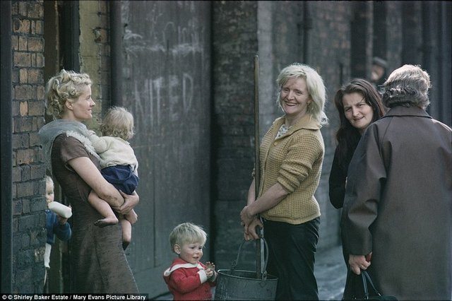 Manchester'da yanmış evlerinin önünde çocuklarıyla bekliyor.  -