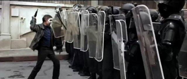 Çeresiz bir adam polis barikatına şemsile ile saldırıyor.