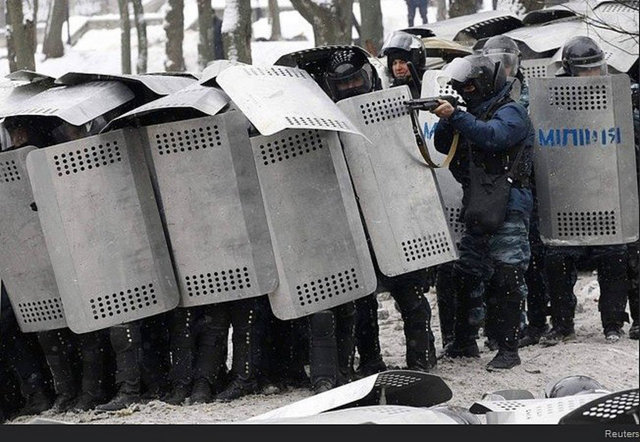 Bir polis memuru elindeki silahı protestoculara doğrulturken..