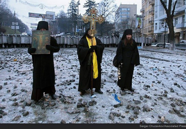 Ortodox rahipler polisler ve protestocular arasında dua ederken.