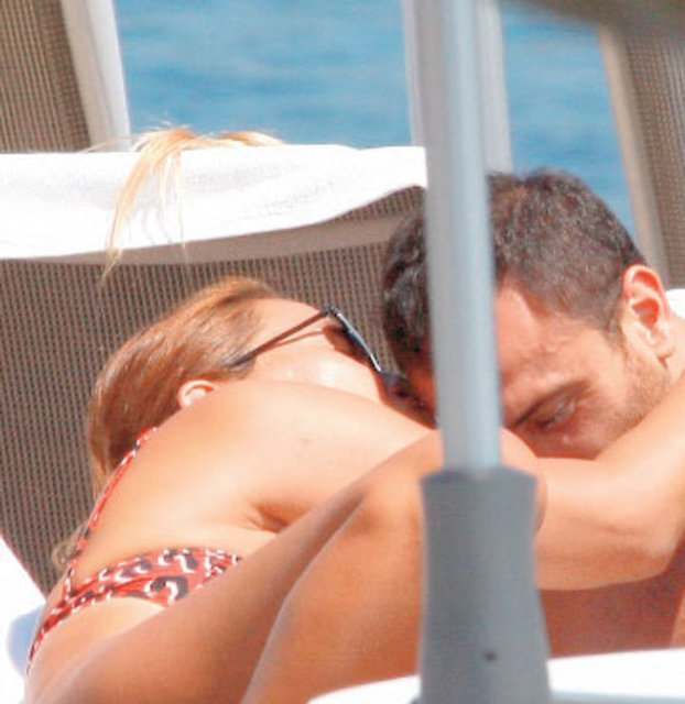 Tatilin keyfini çıkaran karı-koca şezlongda güneşlenirken sırada yaptıkları ayak hareketleri dikkat çekerken Akalın, bir ara kocasına eğilip onu öpücüklere boğdu.