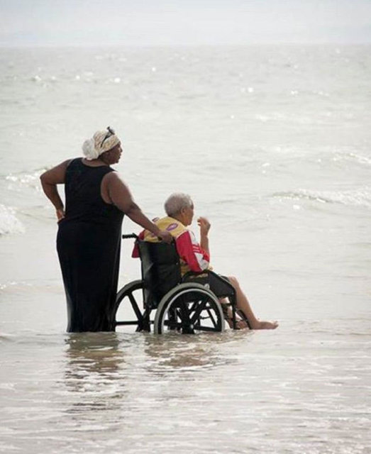 Yürüyemeyen annesini okyanusa getiren bir kadın.