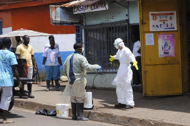 Monrovia'da defin ekibinden biri, görev arkadaşına klor dezenfektan sıkıyor. (20 Ekim 2014, REUTERS/James Giahyue)