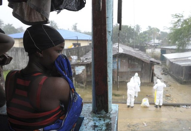 Liberyalı bir kadın; koruyucu kıyafet giymiş sağlık çalışanları Monrovia'daki Duwala pazarında, Ebola belirtileri gösteren kimliği belirlenememiş ölü bir bedeni taşımaya hazırlanırken orada duruyor. (Liberya, 17 Ağustos 2014, REUTERS/2Tango)