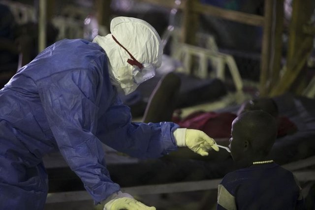 Monrovia'daki Island Kliniği'nde koruyucu ekipman giymiş bir sağlık çalışanı, Ebola tedavisi gören bir hastaya yemek veriyor. (Liberya, 30 Eylül 2014, REUTERS/Christopher Black/WHO)