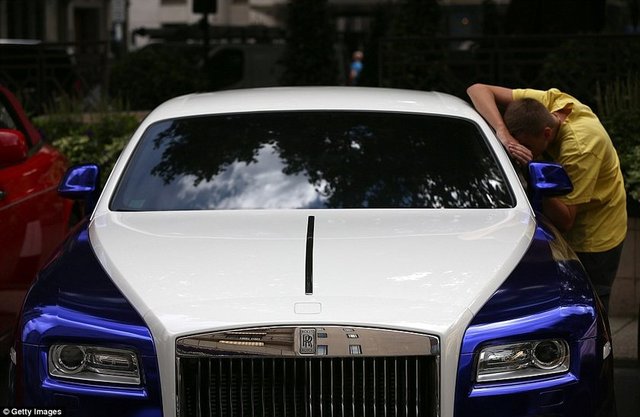 Bir adam Suudi Arabistan plakalı beyaz ve metalik mavi kaplamalı Rolls Royce'un içine bakıyor.  -