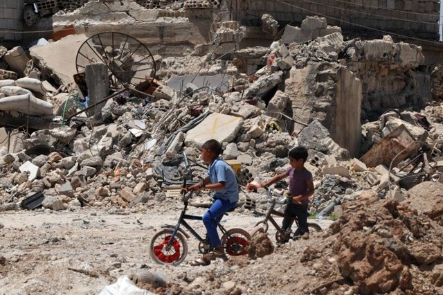 Kentte ilaçlama yapılırken, çocuklar enkazların arasında oyun oynayıp bisiklete binerek eğlenmeye çalışıyor.