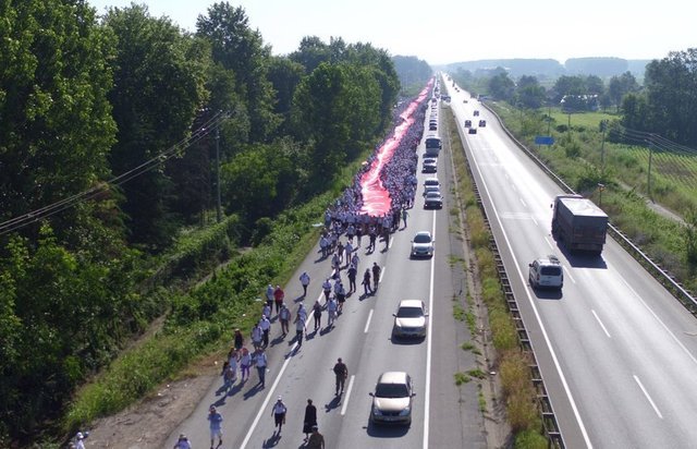 Yol boyuncu uzanan bayrağı on binlerce kişi, sıcak havaya rağmen omuzlarında taşıdı.