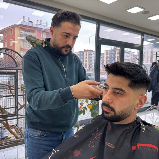 Müşterilerini, omzunda iguana ile tıraş ediyor