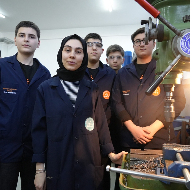 Kadın öğretmen torna tezgahında öğrencilerine üretimi öğretiyor