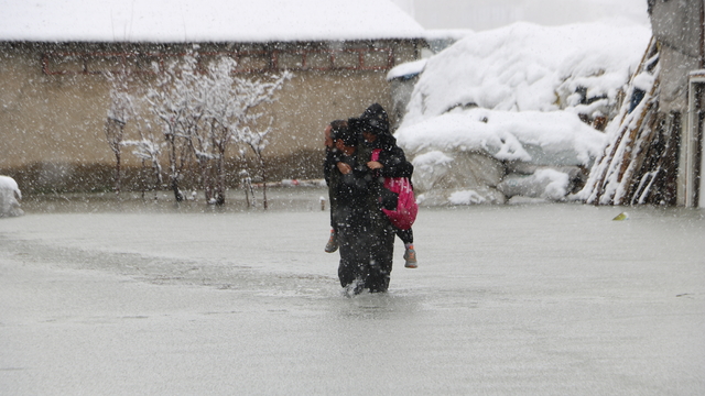 Evinin önünde biriken su nedeniyle çocuklarını sırtında taşıyor