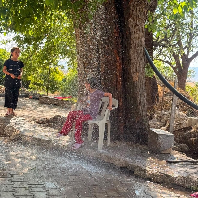 Kavurucu sıcağa karşı çözümü ağaçtan sarkıttığı hortumdan akan suda buldu