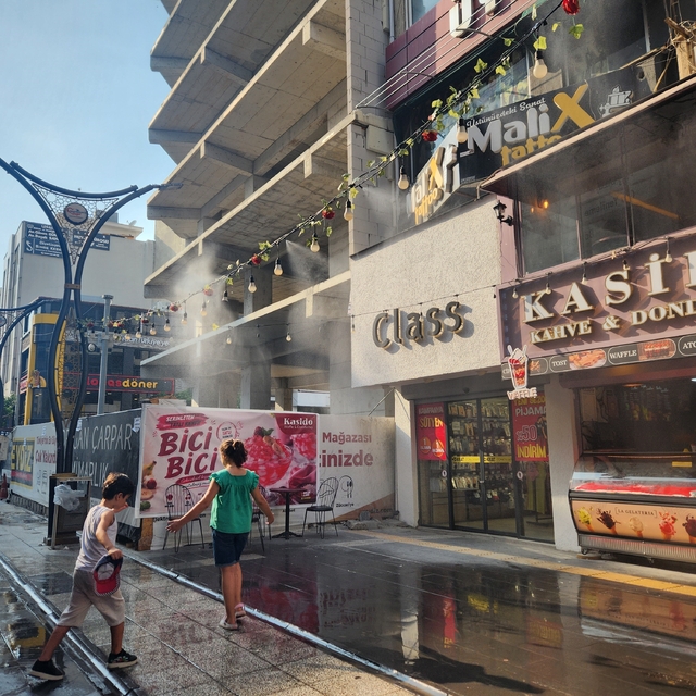 Esnafın iş yerinin önüne kurduğu fıskiye sistemi, kavurucu sıcakta çocuklar...